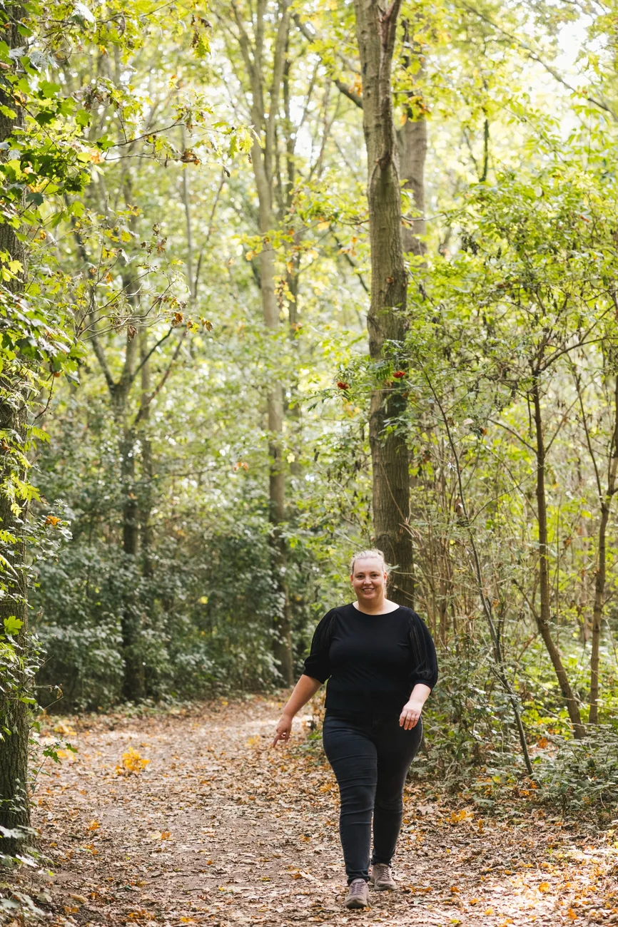 Lindsy wandelt glimlachend over een bospad, met hoge bomen om haar heen.